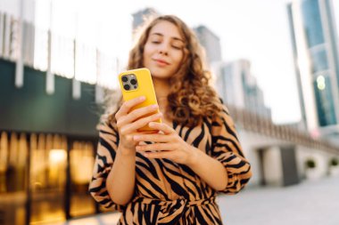 Güneşli bir günde Metropolis 'in arka planına karşı genç bir kadının elindeki parlak renkli telefonun yakın çekimi. Telefon mesajları olan güzel bir kadın, dışarıda geziniyor. Kavram: Turizm, teknoloji.