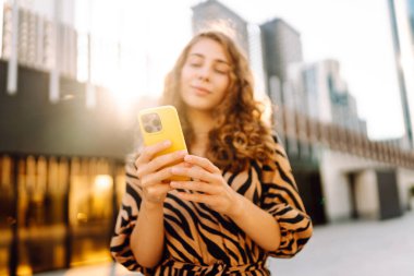 Güneşli bir günde Metropolis 'in arka planına karşı genç bir kadının elindeki parlak renkli telefonun yakın çekimi. Telefon mesajları olan güzel bir kadın, dışarıda geziniyor. Kavram: Turizm, teknoloji.