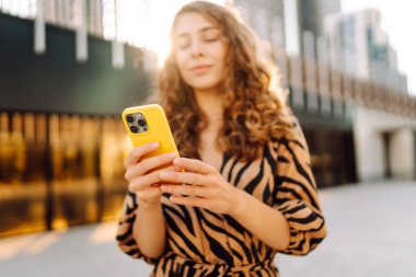 Güneşli bir günde Metropolis 'in arka planına karşı genç bir kadının elindeki parlak renkli telefonun yakın çekimi. Telefon mesajları olan güzel bir kadın, dışarıda geziniyor. Kavram: Turizm, teknoloji.