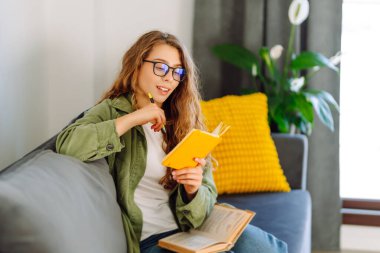 Sarı defterde gözlüklü güzel bir kadının portresi rahat bir odada kanepede otururken. Genç öğrenci rahatlar, evde notlar alır. Eğitim, rahatlama ve konfor kavramı.