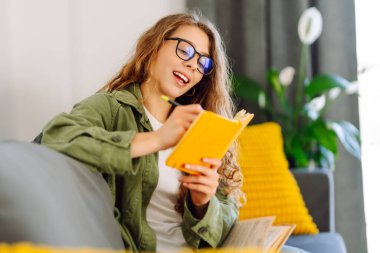 Sarı defterde gözlüklü güzel bir kadının portresi rahat bir odada kanepede otururken. Genç öğrenci rahatlar, evde notlar alır. Eğitim, rahatlama ve konfor kavramı.