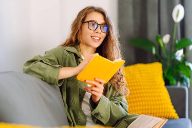 Sarı defterde gözlüklü güzel bir kadının portresi rahat bir odada kanepede otururken. Genç öğrenci rahatlar, evde notlar alır. Eğitim, rahatlama ve konfor kavramı.