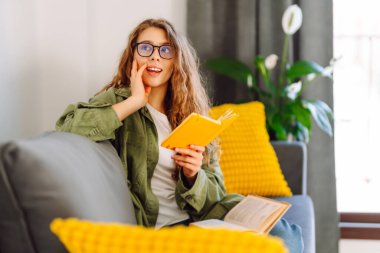 Sarı defterde gözlüklü güzel bir kadının portresi rahat bir odada kanepede otururken. Genç öğrenci rahatlar, evde notlar alır. Eğitim, rahatlama ve konfor kavramı.