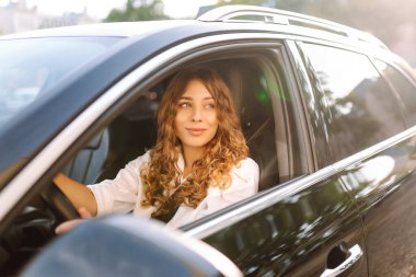 Güneşli bir günde araba süren genç bir kadının portresi. Güzel bir kadın pencereden dışarı bakarak araba sürmekten hoşlanır. Konsept: ulaşım, boş zaman, kentsel.