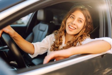 Güneşli bir günde araba süren genç bir kadının portresi. Güzel bir kadın pencereden dışarı bakarak araba sürmekten hoşlanır. Konsept: ulaşım, boş zaman, kentsel.