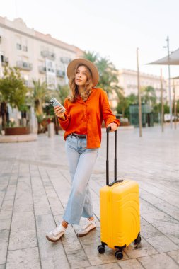 Sarı bavullu ve telefonlu neşeli kadın şehrin mimarisine hayran. Şapkalı ve sırt çantalı bir turist şehrin güneşli caddelerinde geziyor. Turizm kavramları, hafta sonları.