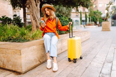 Sarı bavullu ve telefonlu neşeli kadın şehrin mimarisine hayran. Şapkalı ve sırt çantalı bir turist şehrin güneşli caddelerinde geziyor. Turizm kavramları, hafta sonları.