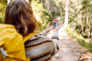 Sırt çantalı kadın yürüyüşçü kayalık yürüyüş yolunda pusula tutuyor. Dişinin arkadan görünüşü pusulaya bakar ve dağların doğal güzelliğinden zevk alır. Seyahat ve seyrüsefer kavramları. Etkin yaşam biçimi.