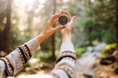 Sırt çantalı kadın yürüyüşçü kayalık yürüyüş yolunda pusula tutuyor. Dişinin arkadan görünüşü pusulaya bakar ve dağların doğal güzelliğinden zevk alır. Seyahat ve seyrüsefer kavramları. Etkin yaşam biçimi.