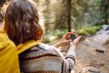 Sırt çantalı kadın yürüyüşçü kayalık yürüyüş yolunda pusula tutuyor. Dişinin arkadan görünüşü pusulaya bakar ve dağların doğal güzelliğinden zevk alır. Seyahat ve seyrüsefer kavramları. Etkin yaşam biçimi.