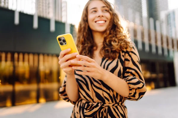 Güneşli bir günde Metropolis 'in arka planına karşı genç bir kadının elindeki parlak renkli telefonun yakın çekimi. Telefon mesajları olan güzel bir kadın, dışarıda geziniyor. Kavram: Turizm, teknoloji.