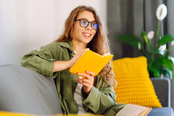 Sarı defterde gözlüklü güzel bir kadının portresi rahat bir odada kanepede otururken. Genç öğrenci rahatlar, evde notlar alır. Eğitim, rahatlama ve konfor kavramı.