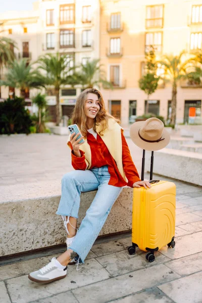 Sarı bavullu ve telefonlu neşeli kadın şehrin mimarisine hayran. Şapkalı ve sırt çantalı bir turist şehrin güneşli caddelerinde geziyor. Turizm kavramları, hafta sonları.