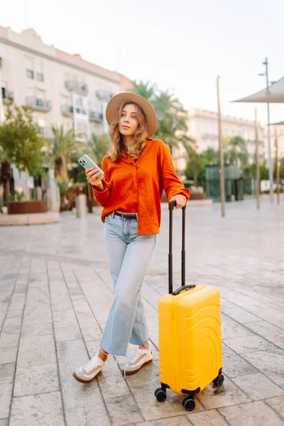 Sarı bavullu ve telefonlu neşeli kadın şehrin mimarisine hayran. Şapkalı ve sırt çantalı bir turist şehrin güneşli caddelerinde geziyor. Turizm kavramları, hafta sonları.