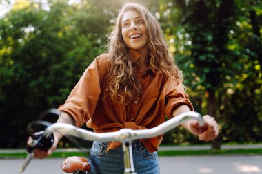 Neşeli bir kadın yeşil bir parkta bir yol boyunca bisiklet sürüyor. Güzel bir kadın güneşli bir günde bisiklet sürmekten hoşlanır. Kavram: rahatlama, yürüyüş, aktif yaşam tarzı.