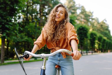 Neşeli bir kadın yeşil bir parkta bir yol boyunca bisiklet sürüyor. Güzel bir kadın güneşli bir günde bisiklet sürmekten hoşlanır. Kavram: rahatlama, yürüyüş, aktif yaşam tarzı.