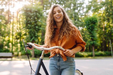 Neşeli bir kadın yeşil bir parkta bir yol boyunca bisiklet sürüyor. Güzel bir kadın güneşli bir günde bisiklet sürmekten hoşlanır. Kavram: rahatlama, yürüyüş, aktif yaşam tarzı.