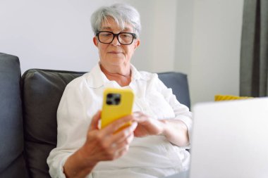 Neşeli yaşlı kadın sahilde duruyor, deniz manzarasına tepeden bakan bir telefonla selfie çekiyor. Mutlu emekliler dışarıda eğleniyor ve blog yazıyor. Blog yazma kavramı, özgürlük. Mutlu emeklilik.