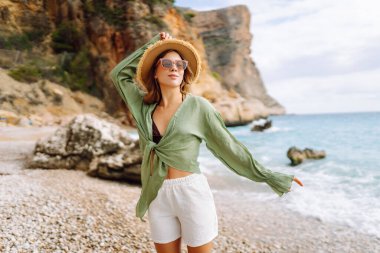 Kumsalda mutlu bir kadın deniz manzarasının tadını çıkarıyor. Hasır şapkalı genç bir kadın kendini özgür hissediyor. Sonsuz denize bakıyor. Özgürlük, doğa ve rahatlama kavramları.