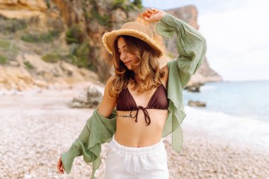 Kumsalda mutlu bir kadın deniz manzarasının tadını çıkarıyor. Hasır şapkalı genç bir kadın kendini özgür hissediyor. Sonsuz denize bakıyor. Özgürlük, doğa ve rahatlama kavramları.