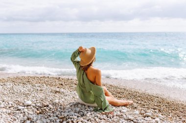 Kumsalda mutlu bir kadın deniz manzarasının tadını çıkarıyor. Hasır şapkalı genç bir kadın kendini özgür hissediyor. Sonsuz denize bakıyor. Özgürlük, doğa ve rahatlama kavramları.