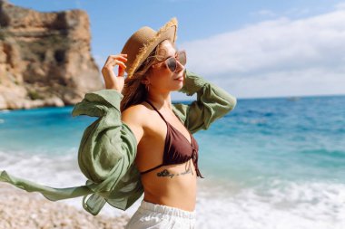 Kumsalda mutlu bir kadın deniz manzarasının tadını çıkarıyor. Hasır şapkalı genç bir kadın kendini özgür hissediyor. Sonsuz denize bakıyor. Özgürlük, doğa ve rahatlama kavramları.