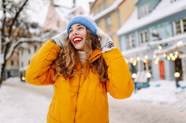 Parlak ceketli ve kırmızı rujlu mutlu kadın karlı şehir caddesinde yeni yağmış karı elinde tutuyor. Güzel bir turist şehir dışında dolaşmaktan hoşlanır. Kavram: Turizm, eğlence, kış.