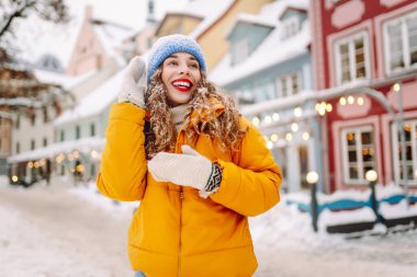 Parlak ceketli ve kırmızı rujlu mutlu kadın karlı şehir caddesinde yeni yağmış karı elinde tutuyor. Güzel bir turist şehir dışında dolaşmaktan hoşlanır. Kavram: Turizm, eğlence, kış.