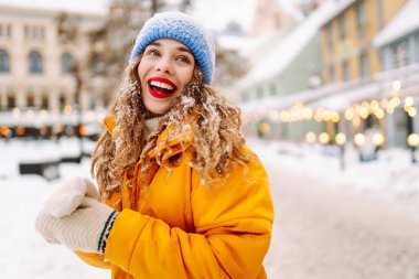 Parlak ceketli ve kırmızı rujlu mutlu kadın karlı şehir caddesinde yeni yağmış karı elinde tutuyor. Güzel bir turist şehir dışında dolaşmaktan hoşlanır. Kavram: Turizm, eğlence, kış.
