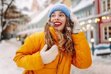 Parlak ceketli ve kırmızı rujlu mutlu kadın karlı şehir caddesinde yeni yağmış karı elinde tutuyor. Güzel bir turist şehir dışında dolaşmaktan hoşlanır. Kavram: Turizm, eğlence, kış.