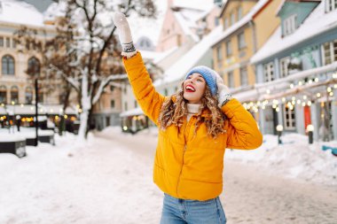 Parlak ceketli ve kırmızı rujlu mutlu kadın karlı şehir caddesinde yeni yağmış karı elinde tutuyor. Güzel bir turist şehir dışında dolaşmaktan hoşlanır. Kavram: Turizm, eğlence, kış.