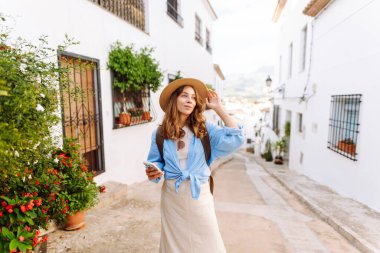 Şapkalı güzel bir kadın kalabalık bir meydanda duruyor, elinde telefon var. Güneş gözlüklü genç bir turist güneşli günün tadını çıkarıyor ve dışarıda blog yazıyor. Konsept: turizm, eğlence ve yaşam tarzı.