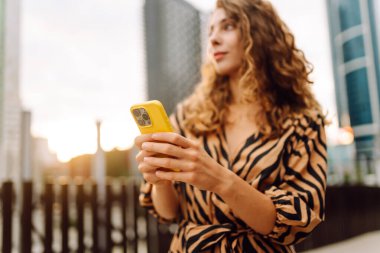 Elinde telefon olan genç bir kadının portresi metropolün arka planında duruyor. Güzel bir kadın telefonuyla mesaj atıyor ve büyük bir şehirde gezmekten zevk alıyor. Kavram: kentsel, turizm ve blog yazarlığı.