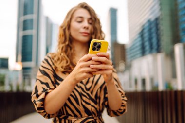 Elinde telefon olan genç bir kadının portresi metropolün arka planında duruyor. Güzel bir kadın telefonuyla mesaj atıyor ve büyük bir şehirde gezmekten zevk alıyor. Kavram: kentsel, turizm ve blog yazarlığı.