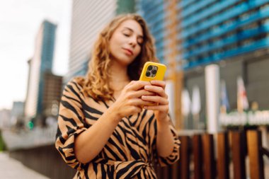 Elinde telefon olan genç bir kadının portresi metropolün arka planında duruyor. Güzel bir kadın telefonuyla mesaj atıyor ve büyük bir şehirde gezmekten zevk alıyor. Kavram: kentsel, turizm ve blog yazarlığı.