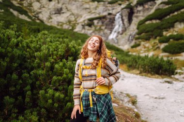 Güneşli bir günde dağlarda yürüyüş parkurunda sırt çantasıyla gezen güzel bir kadın. Dişi bir yürüyüşçü dağ manzarasından zevk alır. Doğa, macera ve yürüyüş kavramları.