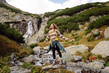 Güneşli bir günde dağlarda yürüyüş parkurunda sırt çantasıyla gezen güzel bir kadın. Dişi bir yürüyüşçü dağ manzarasından zevk alır. Doğa, macera ve yürüyüş kavramları.