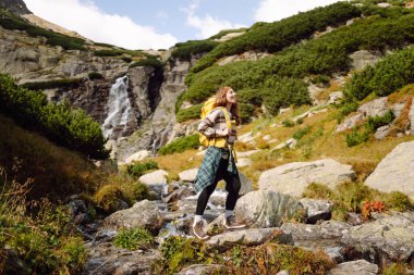 Güneşli bir günde dağlarda yürüyüş parkurunda sırt çantasıyla gezen güzel bir kadın. Dişi bir yürüyüşçü dağ manzarasından zevk alır. Doğa, macera ve yürüyüş kavramları.