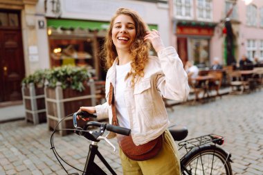 Neşeli bir kadın güneşli şehir sokaklarında bisiklet sürüyor. Genç bir turist dışarıda bisiklet sürerek eğleniyor. Konsept: Hafta sonu, turizm. Etkin yaşam biçimi.