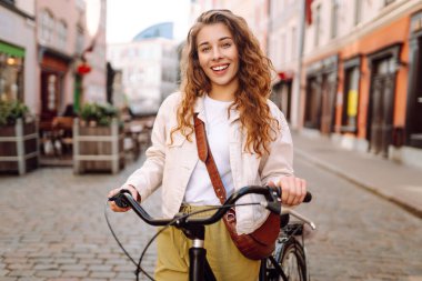 Neşeli bir kadın güneşli şehir sokaklarında bisiklet sürüyor. Genç bir turist dışarıda bisiklet sürerek eğleniyor. Konsept: Hafta sonu, turizm. Etkin yaşam biçimi.