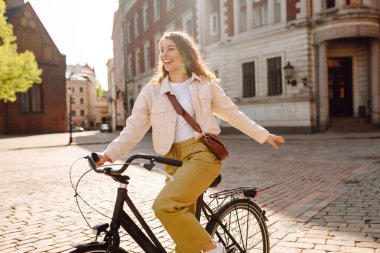 Neşeli bir kadın güneşli şehir sokaklarında bisiklet sürüyor. Genç bir turist dışarıda bisiklet sürerek eğleniyor. Konsept: Hafta sonu, turizm. Etkin yaşam biçimi.