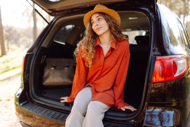 Güneş gözlüklü bir gezgin gün batımında arabanın bagajında oturur. Güzel bir kadın doğada yolculuk yapmaktan hoşlanır. Macera kavramı, ulaşım, aktif yaşam tarzı.