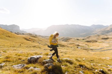 Sarı sırt çantalı güzel bir bayan yürüyüşçü dağ sırtında durup günbatımını izliyor. Genç kadın yolculuğun tadını çıkarıyor ve gün batımının özgürlüğünü hissediyor. Yürüyüş, özgürlük ve aktif yaşam tarzı kavramı.