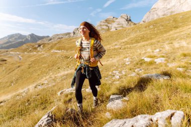 Sarı sırt çantalı güzel bir bayan yürüyüşçü dağ sırtında durup günbatımını izliyor. Genç kadın yolculuğun tadını çıkarıyor ve gün batımının özgürlüğünü hissediyor. Yürüyüş, özgürlük ve aktif yaşam tarzı kavramı.