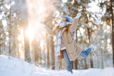 Gülümseyen bir kadın karlı bir ormanda eğleniyor. Tatlı bir kadın güneşli bir parkta kar atarak kış gününün tadını çıkarır. Yürüyüş kavramı, soğuk. Yaşam biçimi.