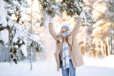 Gülümseyen bir kadın karlı bir ormanda eğleniyor. Tatlı bir kadın güneşli bir parkta kar atarak kış gününün tadını çıkarır. Yürüyüş kavramı, soğuk. Yaşam biçimi.