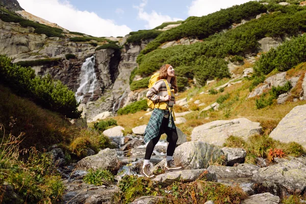 Güneşli bir günde dağlarda yürüyüş parkurunda sırt çantasıyla gezen güzel bir kadın. Dişi bir yürüyüşçü dağ manzarasından zevk alır. Doğa, macera ve yürüyüş kavramları.