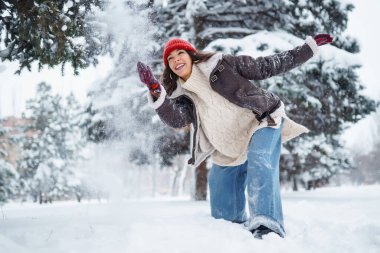 Kırmızı şapkalı neşeli kadın eğleniyor ve karlı parkta kar atıyor. Güzel bir kadın kış gününden ve dışarıda vakit geçirmekten hoşlanır. Doğanın kavramsal tasviri, eğlence ve rahatlama.