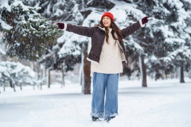 Kırmızı şapkalı neşeli kadın eğleniyor ve karlı parkta kar atıyor. Güzel bir kadın kış gününden ve dışarıda vakit geçirmekten hoşlanır. Doğanın kavramsal tasviri, eğlence ve rahatlama.