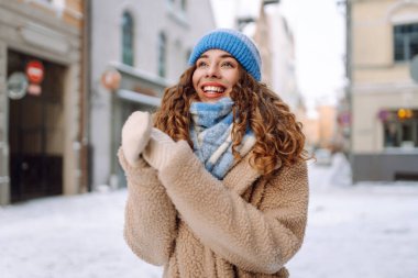 Eşarp ve şapkaya sarılmış mutlu bir kadın güneşli bir günde karlı bir sokakta duruyor. Şık giyinmiş genç bir turist dondurucu havanın tadını çıkarıyor. Yürüme, tarz ve moda kavramı..